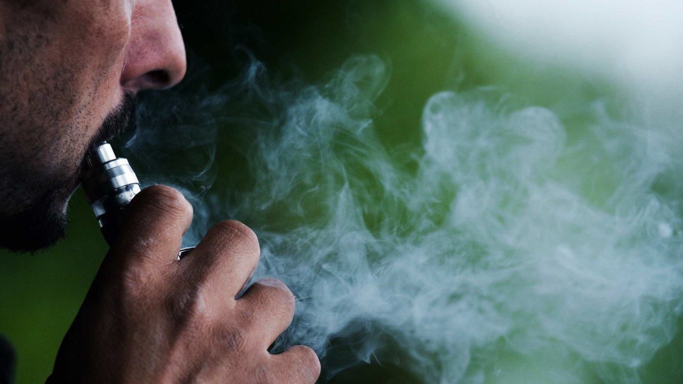 side profilie of a man vaping with smoke clouds